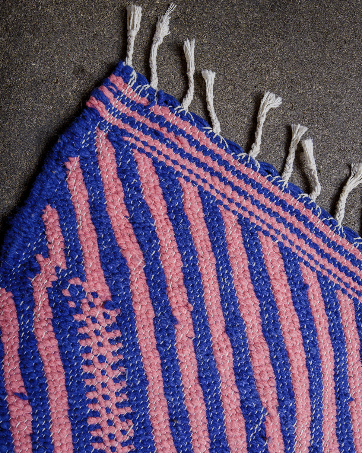 Corner of Kelim rug made of blue and pink wool with white cotton tassels.